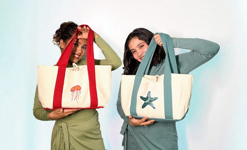 Two models holding Island Days canvas beach totes with beaded jellyfish and starfish motifs